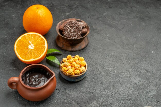 Horizontal view of set of whole and cut in half fresh oranges and biscuits on dark table