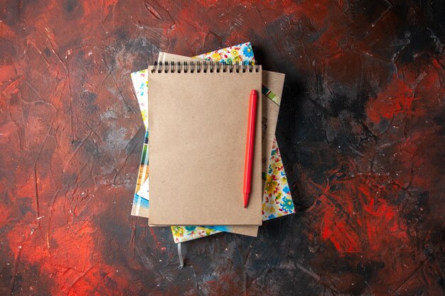 Horizontal view of several stacked spiral notebooks with pen on dark background