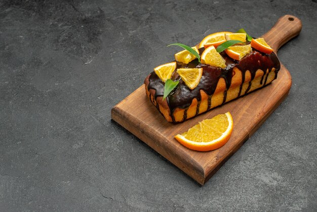 黒いテーブルのまな板にオレンジとチョコレートで飾られたおいしいケーキの水平方向のビュー