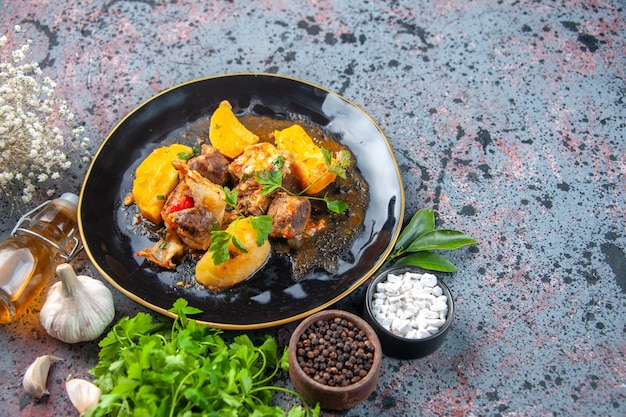 Horizontal view of tasty dinner with meat potatoes served with green in a black plate and spices garlic oil bottle