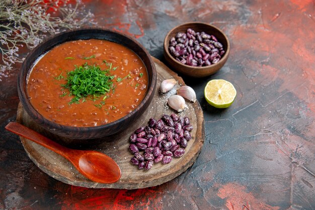 Horizontal view of tomato soup beans garlic on wooden cutting board and spoon on mix color table