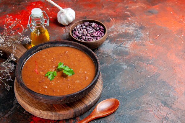 Horizontal view of tomato soup on a brown cutting board and oil bottle on a mixed color table