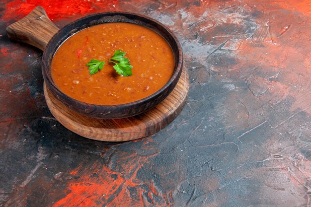 Horizontal view of tomato soup on a brown cutting board on the right side of a mixed color table