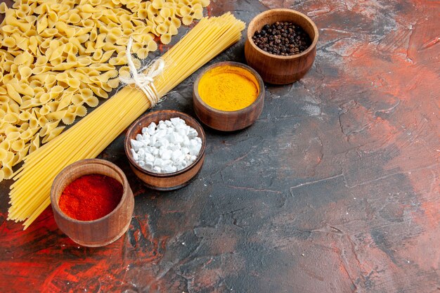 Horizontal view of uncooked pasta in various forms and different spices on black table
