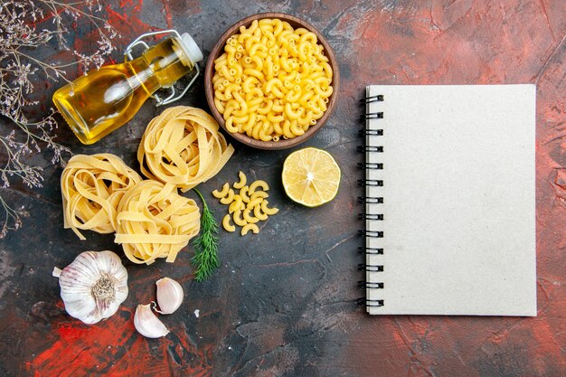 Horizontal view of uncooked three portions of spaghetti green oil bottle and notebook on mixed color table