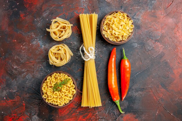 Horizontal view of various types of uncooked pastas and peppers on mixed color table