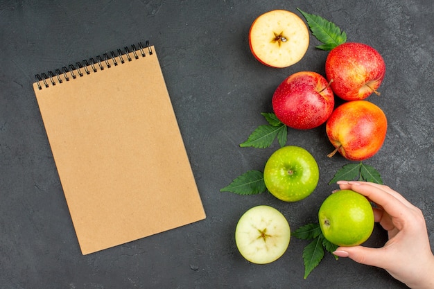 Horizontal view of whole and cut fresh natural apples and leaves and notebook on black background