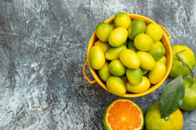 Horizontal view of a yellow bucket full of fresh green tangerines and cut in half tangerines on the right side of gray background