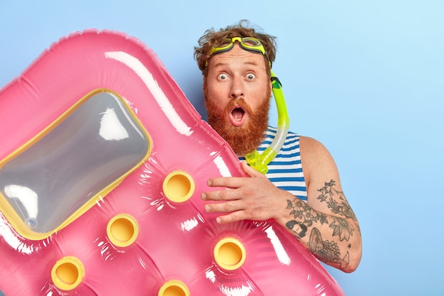 Foto gratuita uomo con la barba rossa inorridito in posa con articoli da spiaggia