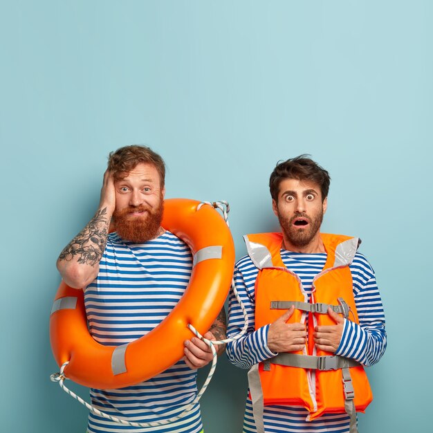 Horrified guys posing at the beach with lifejacket and lifebuoy