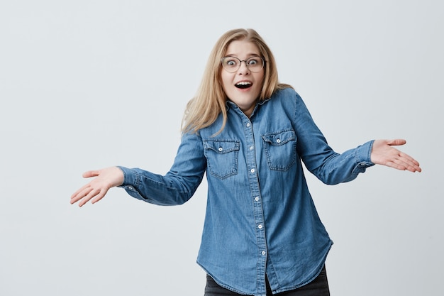 Horrified woman with blonde hair and eyeglasses gestures in puzzlement, being shocked, surprised as remembers that she forgot to pay bills. Frustrated female with bugged eyes exclaims in panic