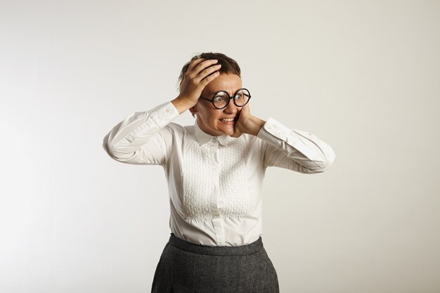 Horrified young woman holds her head in her hands and looks into distance isolated on white