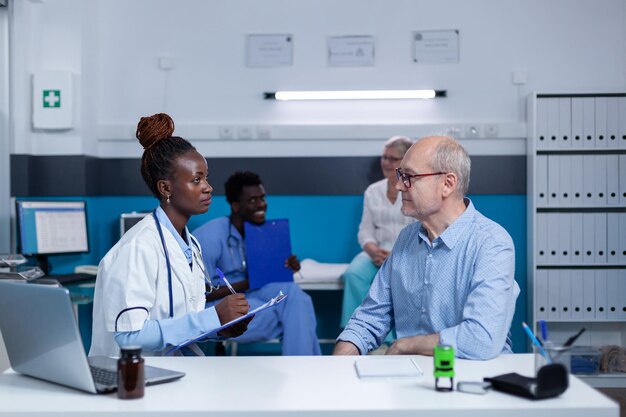 Hospital medic expert writing down sick senior patient illness symptoms while prescribing antibiotic medicine. Clinic specialist analyzing patient condition and offering treatment for disease