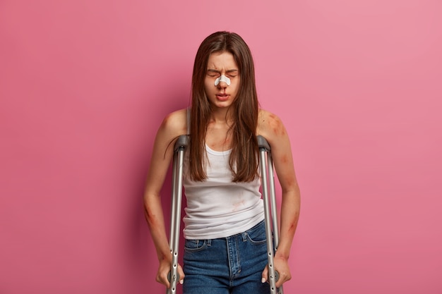 Foto gratuita la donna ricoverata ha un periodo di riabilitazione dopo un grave incidente, varie fratture, posa con le stampelle, soffre di gravi malattie della colonna vertebrale, ferita dopo un incidente d'auto, ha rotto il naso sanguinante