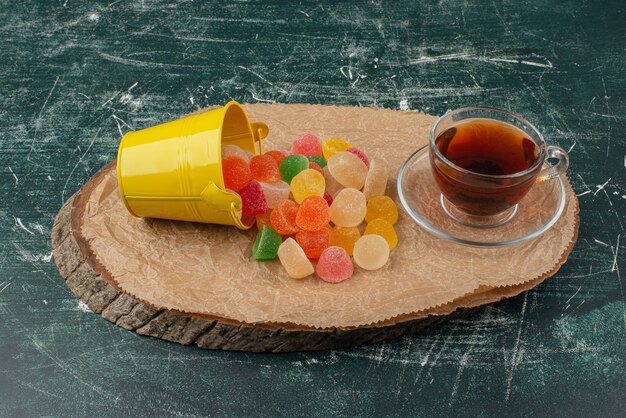 Hot, aroma tea with yellow bucket of jelly candies on wooden board