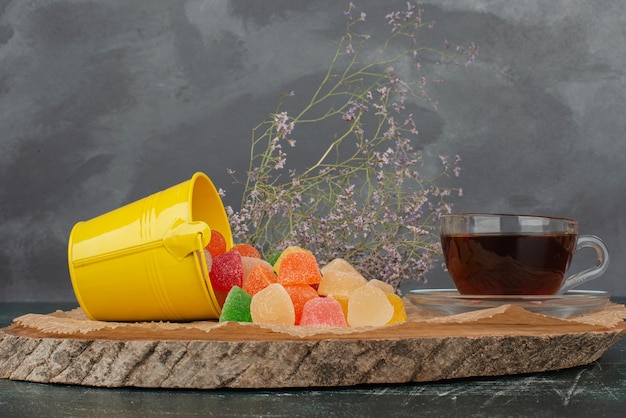 Free photo hot, aroma tea with yellow bucket of jelly candies on wooden board