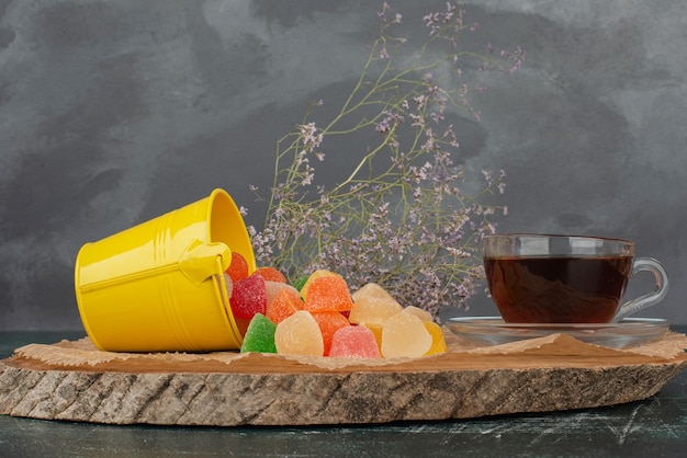 Hot, aroma tea with yellow bucket of jelly candies on wooden board