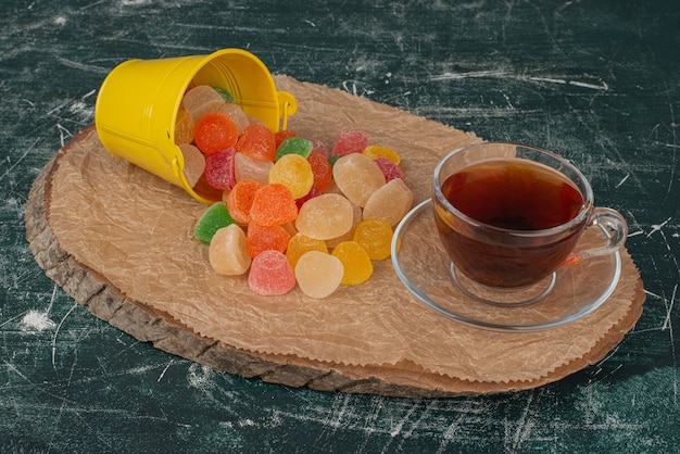 Бесплатное фото Горячий ароматный чай с желтым ведром желейных конфет на деревянной доске