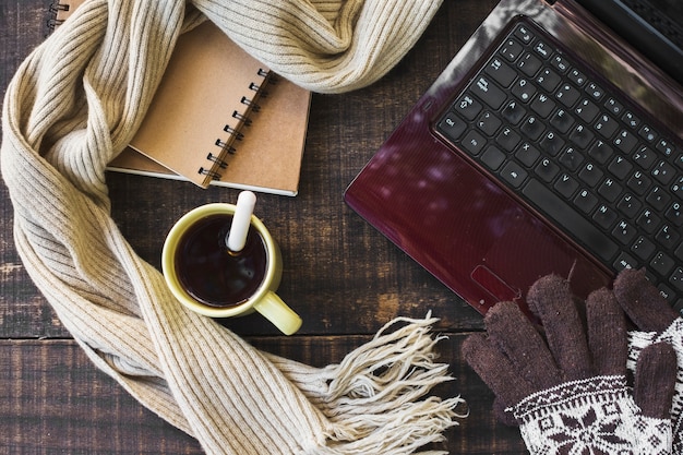 Hot beverage and warm clothes near laptop and notebooks