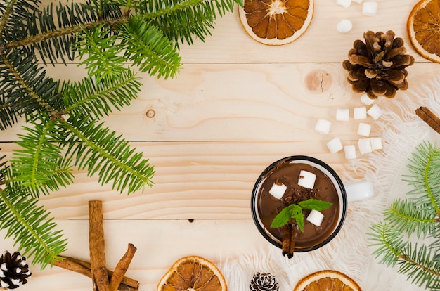 Hot chocolate on desk with marshmallows, oranges and spruce bumps