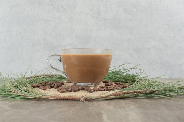 Hot coffee, pine grass and coffee beans on marble surface. 