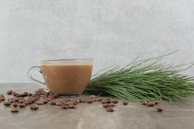 Горячий кофе, сосновая трава и кофейные зерна на мраморном столе