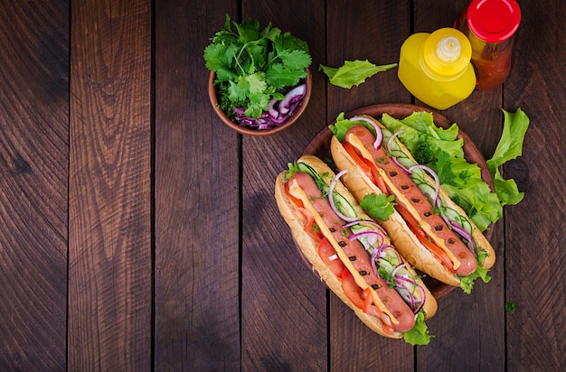 Hot dog with  sausage, cucumber, tomato and lettuce on dark wooden table. Summer hotdog. Top view