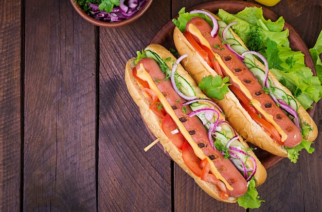 Hot dog with  sausage, cucumber, tomato and lettuce on dark wooden table. Summer hotdog. Top view