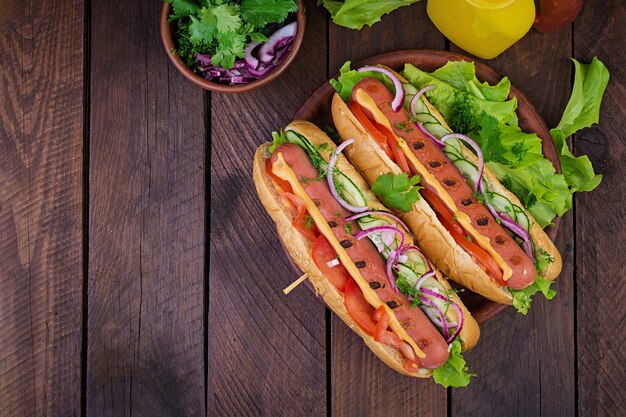 Hot dog with  sausage, cucumber, tomato and lettuce on dark wooden table. Summer hotdog. Top view