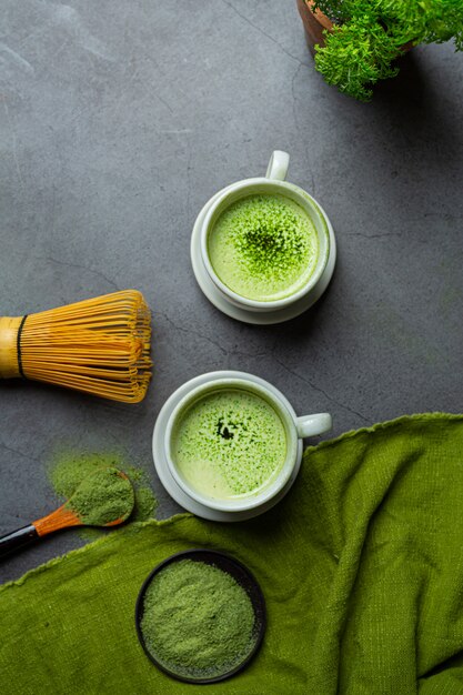 Hot green tea in a glass with cream topped with green tea, decorated with green tea powder.