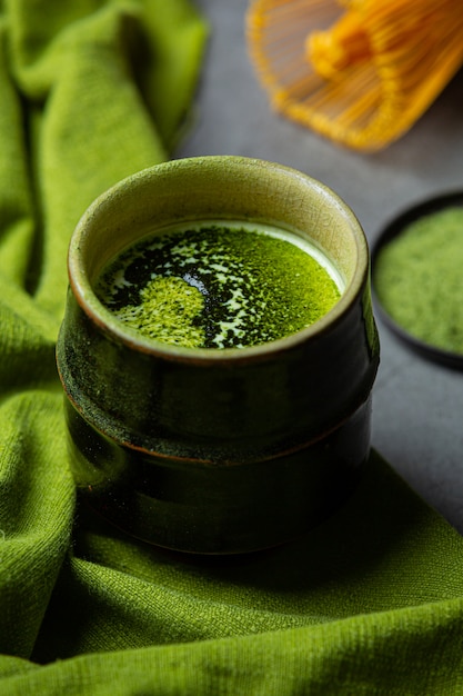 Tè verde caldo in un bicchiere con crema condita con tè verde, decorato con tè verde in polvere.
