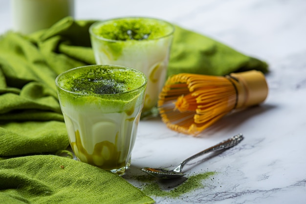 Hot green tea in a glass with cream topped with green tea, decorated with green tea powder.