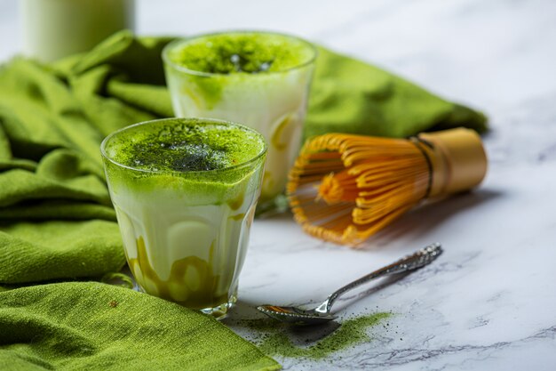 Hot green tea in a glass with cream topped with green tea, decorated with green tea powder.