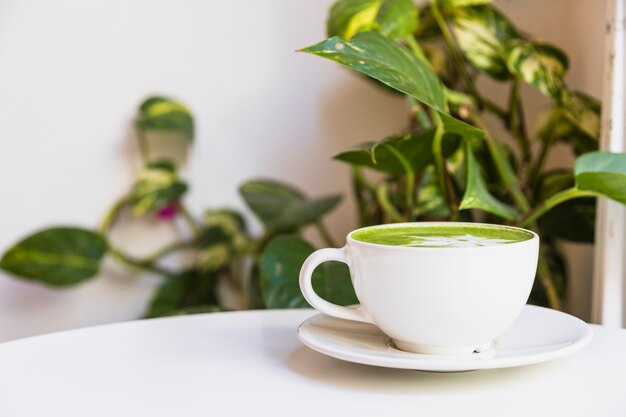 Hot matcha green tea in cup on saucer over the white table