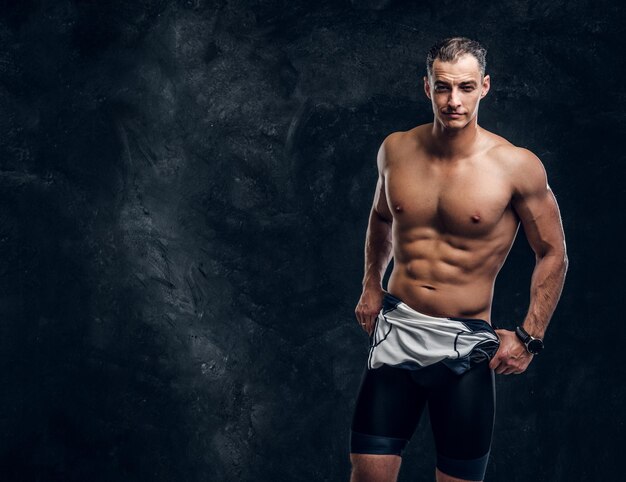 Hot sexy fit man is taking off his wetsuit in dark photo studio.