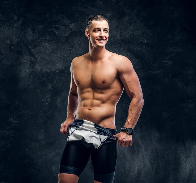 Hot sexy fit man is taking off his wetsuit in dark photo studio.