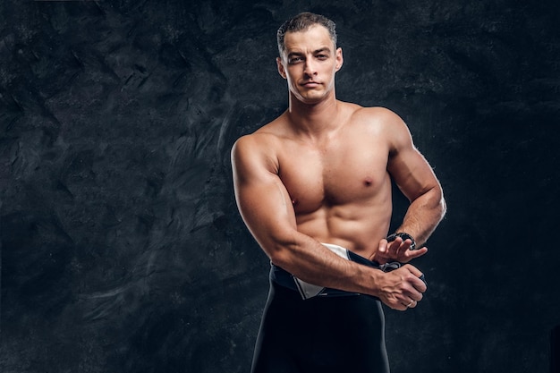 Hot sexy fit man is taking off his wetsuit in dark photo studio.