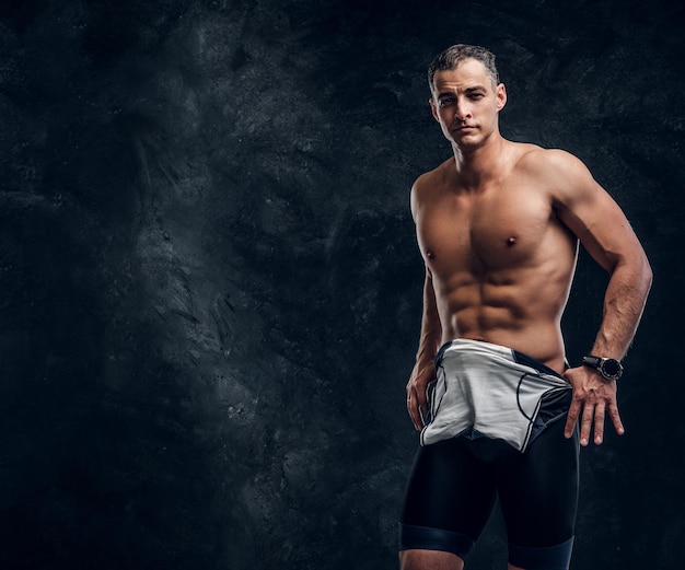 Hot sexy fit man is taking off his wetsuit in dark photo studio.