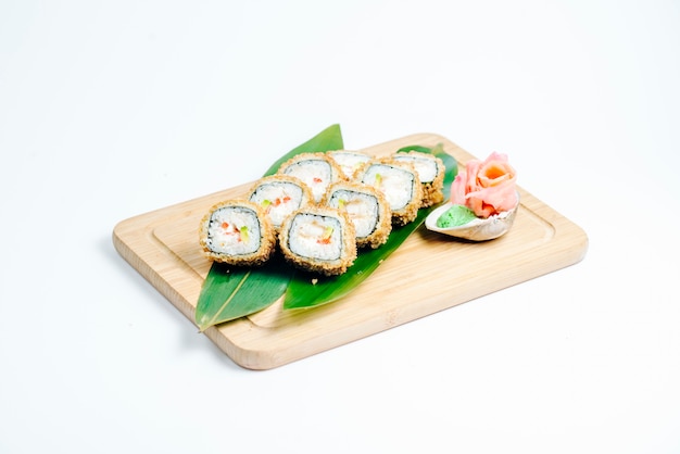 Hot sushi rolls with tempura and avocado served on leaves on wood board