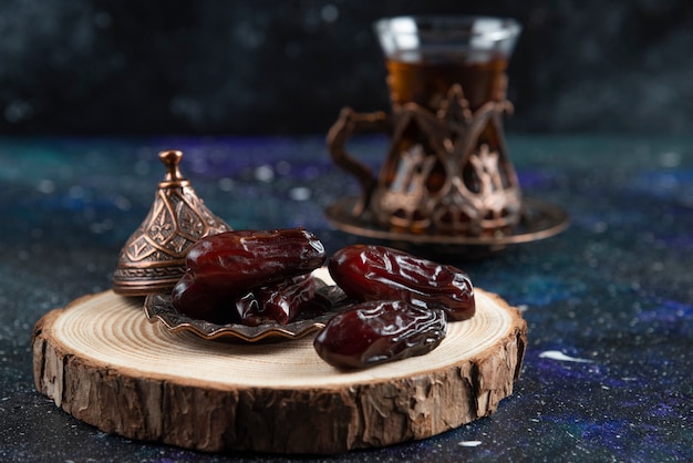 Hot tea behind of dry dates on blue surface