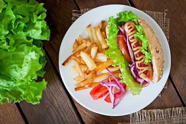 Hotdog with ketchup mustard and lettuce on wooden table.