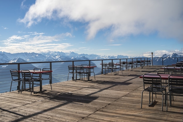 Hotel balcony with tables and chairs overlooking surrounding Alps and lakes on a cloudy day
