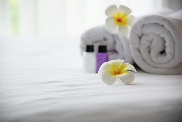 Hotel towel and shampoo and soap bath bottle set on white bed with plumeria flower decorated - relax vacation at the hotel resort concept