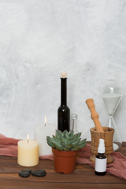 Hour glass; cactus plant; lighted candle; lastone; essential oil; wooden mortar and pastel on table against wall