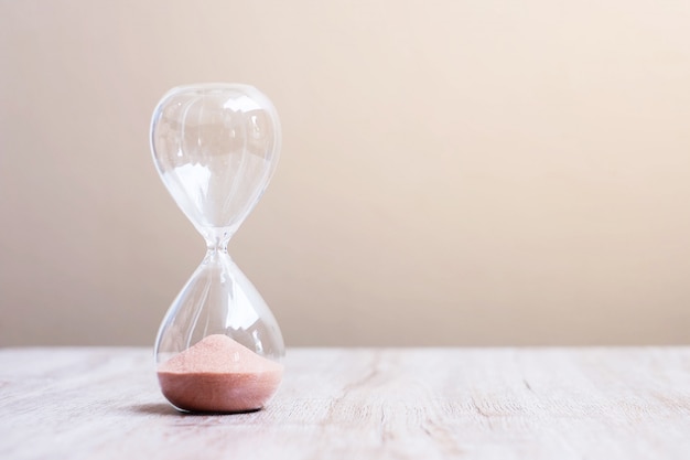 Hourglass on table, sand flowing through the bulb of sandglass measuring the passing time. countdown, deadline, life time and retirement concept