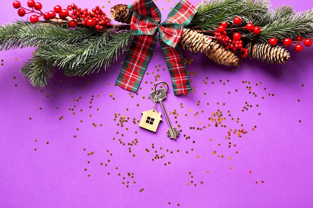 House key with keychain cottage on a festive background with christmas tree, lights of garlands. happy new year-purple background, gift, greeting card. purchase, construction, relocation, mortgage