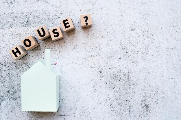 House model blocks with question mark sign over the paper model against grunge white wall