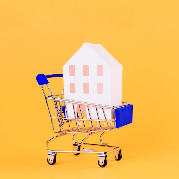 黄色の背景に対してショッピングカート内の家モデル