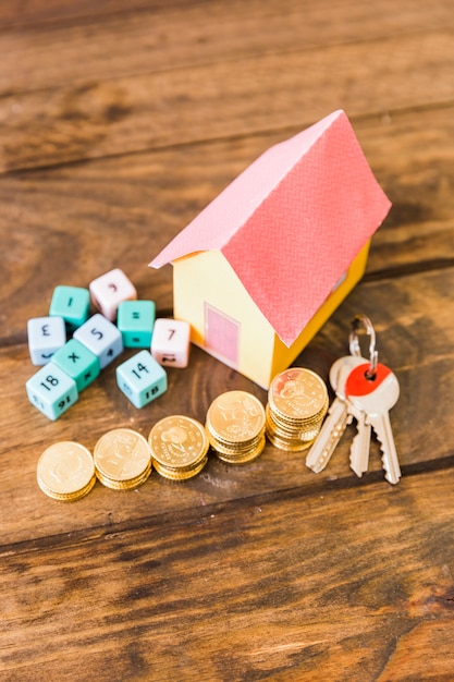 Модель дома, ключ, математические блоки и уложенные монеты на деревянном фоне