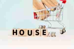 Free photo house wooden blocks with stack of coins in front of house model in the shopping cart